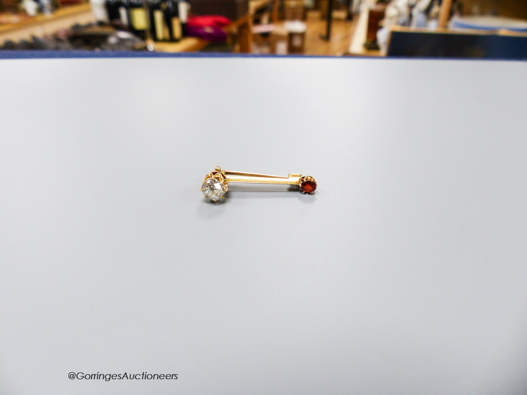 A small yellow metal, cushion cut diamond and garnet? set two stone bar brooch, 30mm, gross weight 3.1 grams